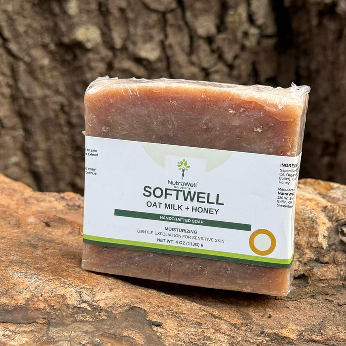 SoftWell Oat Milk + Honey soap bar resting on natural stone beside a tree